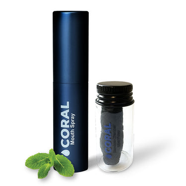 An image featuring a blue cylindrical bottle labeled 'CORAL Mouth Spray' standing next to a clear glass vial with a black lid, both with the brand 'CORAL' visible. There are also a few leaves of mint included for scale.