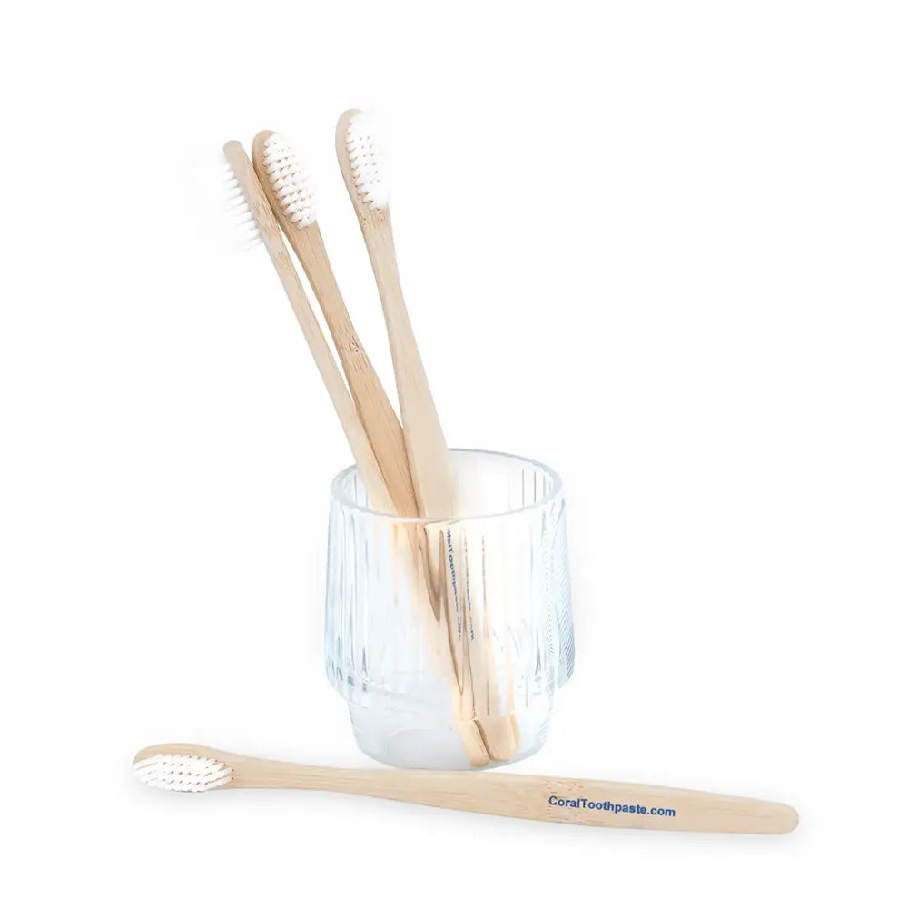 Eco-friendly Coral bamboo toothbrushes with soft white bristles in a glass cup, promoting sustainable, biodegradable oral care with natural bamboo handles for a plastic-free dental routine.